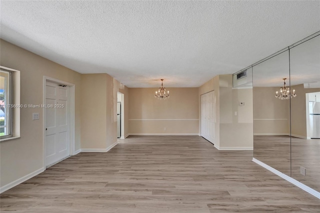 unfurnished room featuring an inviting chandelier, visible vents, light wood finished floors, and a textured ceiling