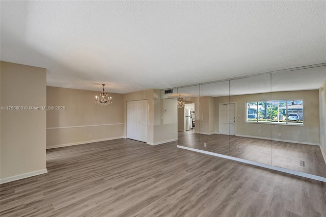 unfurnished living room with a textured ceiling, baseboards, wood finished floors, and a notable chandelier