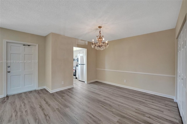 empty room featuring an inviting chandelier, a textured ceiling, baseboards, and wood finished floors