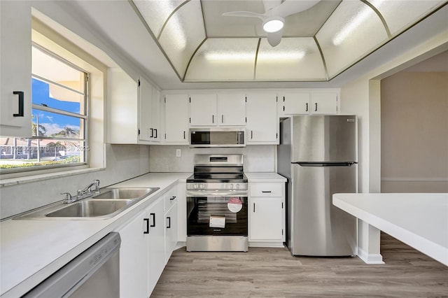 kitchen with white cabinets, a raised ceiling, appliances with stainless steel finishes, light countertops, and a sink