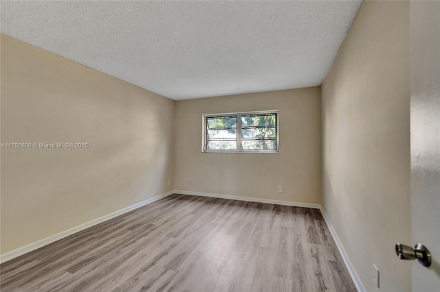 empty room featuring a textured ceiling, wood finished floors, and baseboards