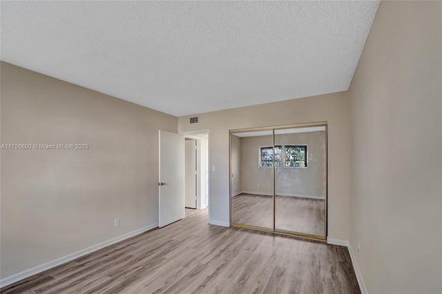 unfurnished bedroom with baseboards, a closet, visible vents, and wood finished floors