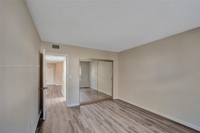 unfurnished bedroom with visible vents, a textured ceiling, baseboards, and wood finished floors