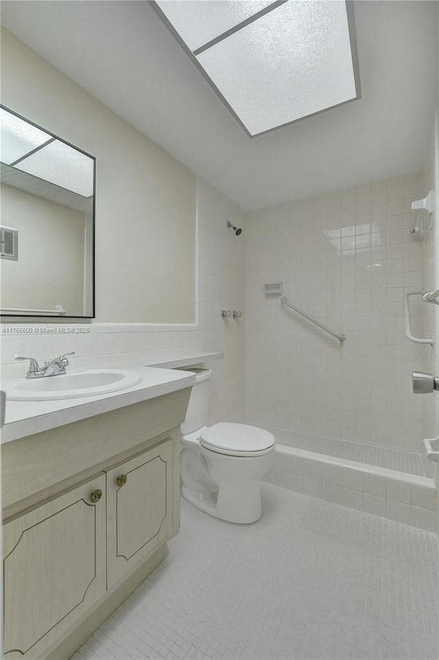 bathroom with tiled shower, toilet, tile patterned flooring, vanity, and tile walls