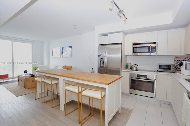 kitchen featuring a toaster, white cabinetry, appliances with stainless steel finishes, a kitchen bar, and rail lighting