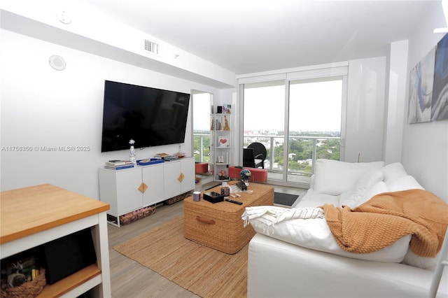 living room with light wood-type flooring, visible vents, and a wall of windows