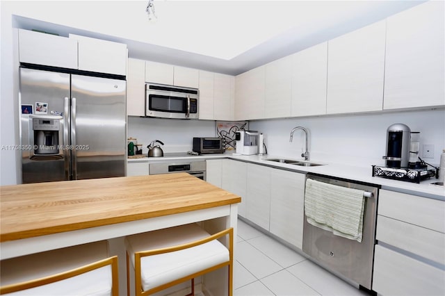 kitchen featuring a toaster, appliances with stainless steel finishes, white cabinetry, a sink, and light tile patterned flooring