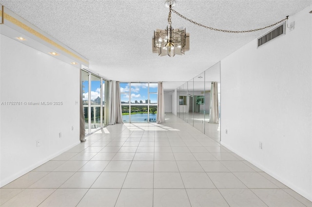 empty room featuring floor to ceiling windows, visible vents, a textured ceiling, and light tile patterned floors