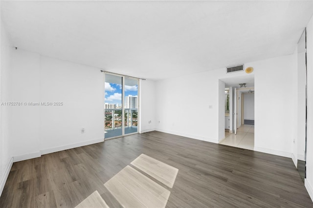 unfurnished room featuring baseboards, visible vents, wood finished floors, a view of city, and a wall of windows