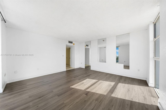 empty room featuring wood finished floors, visible vents, and baseboards