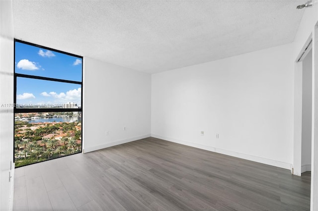 empty room with baseboards, wood finished floors, a water view, a textured ceiling, and floor to ceiling windows