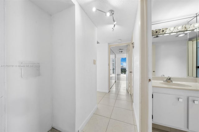 hallway with track lighting, light tile patterned flooring, a sink, and baseboards