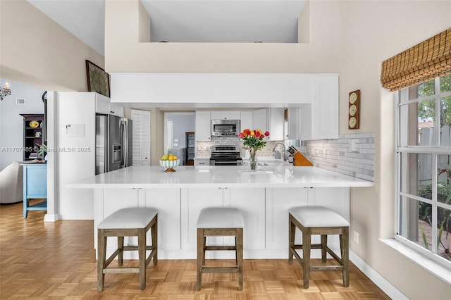 kitchen with stainless steel appliances, a high ceiling, a peninsula, white cabinetry, and light countertops