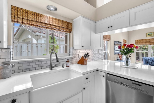 kitchen featuring white cabinets, decorative backsplash, light countertops, stainless steel dishwasher, and a sink