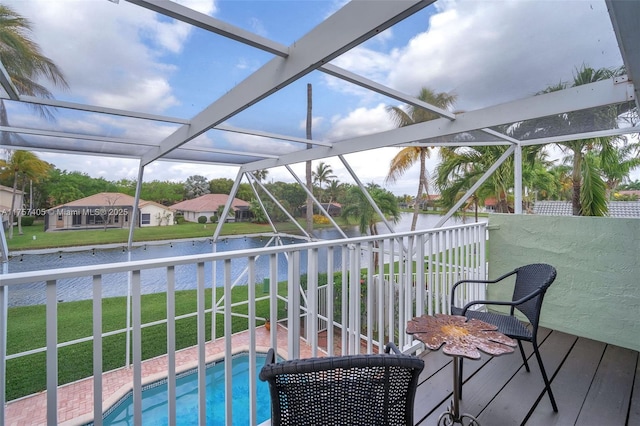 pool featuring glass enclosure, a lawn, and a water view