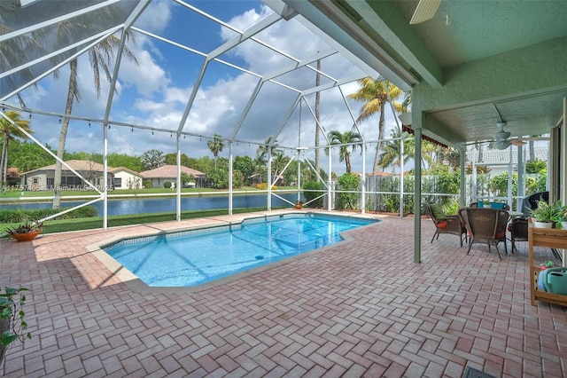 outdoor pool with glass enclosure, a patio area, a water view, and ceiling fan