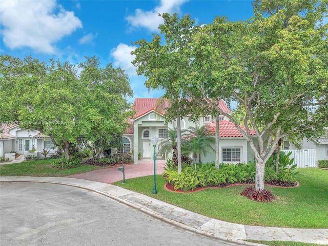 view of front of house with a tile roof, fence, decorative driveway, a front lawn, and stucco siding