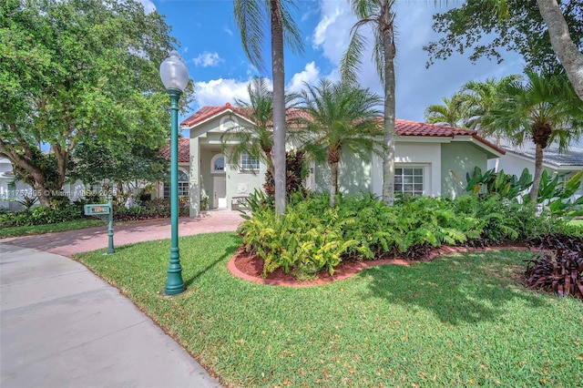 mediterranean / spanish house featuring a front yard, decorative driveway, a tile roof, and stucco siding