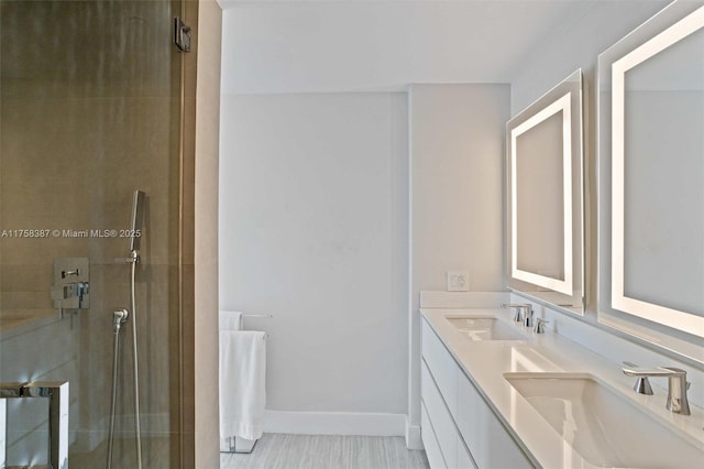 full bath with double vanity, a shower with door, baseboards, and a sink