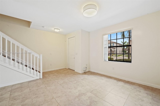 empty room with tile patterned floors, baseboards, and stairs