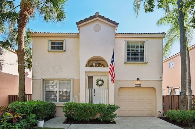 mediterranean / spanish house with stucco siding, an attached garage, concrete driveway, and fence