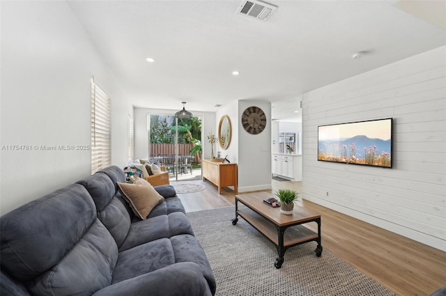 living room with visible vents, light wood finished floors, recessed lighting, wood walls, and an accent wall