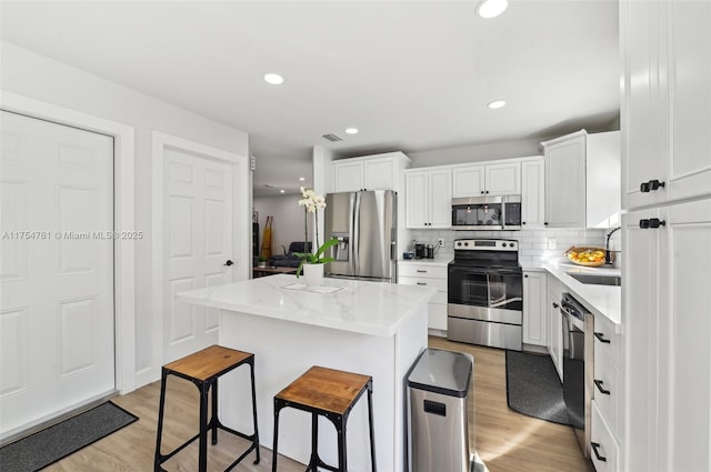 kitchen with light wood finished floors, a center island, a breakfast bar area, appliances with stainless steel finishes, and a sink