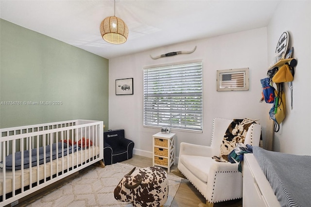 bedroom with baseboards, a nursery area, and wood finished floors