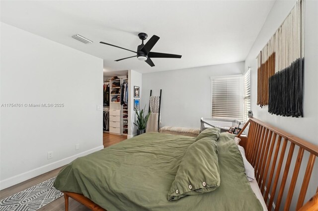 bedroom featuring a spacious closet, visible vents, baseboards, wood finished floors, and a closet