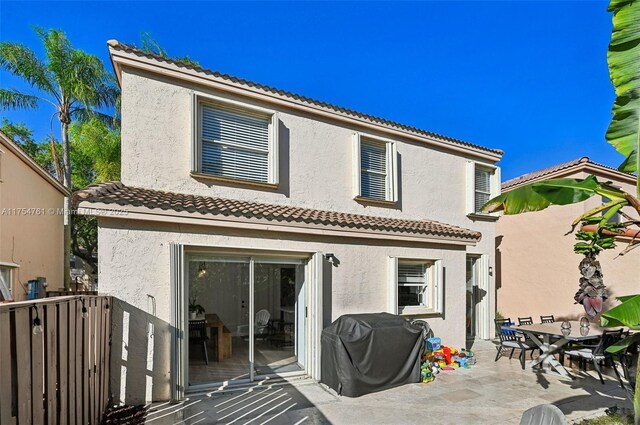 rear view of property with stucco siding, a patio, fence, and a tiled roof