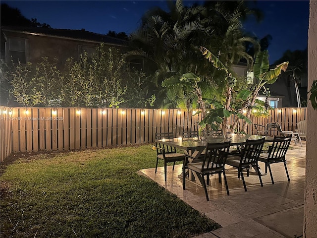 yard at twilight featuring outdoor dining space, a patio area, and a fenced backyard