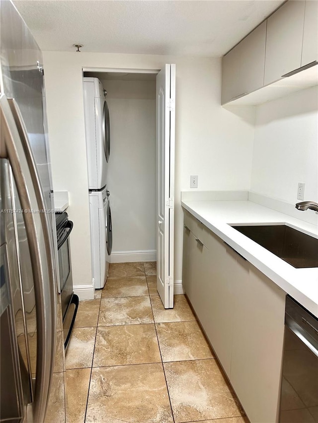 kitchen featuring stacked washer and dryer, stainless steel dishwasher, a sink, and light countertops