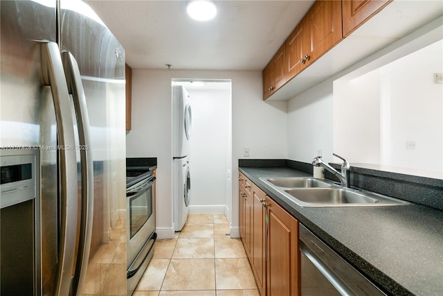 kitchen with a sink, appliances with stainless steel finishes, brown cabinets, dark countertops, and stacked washer and clothes dryer