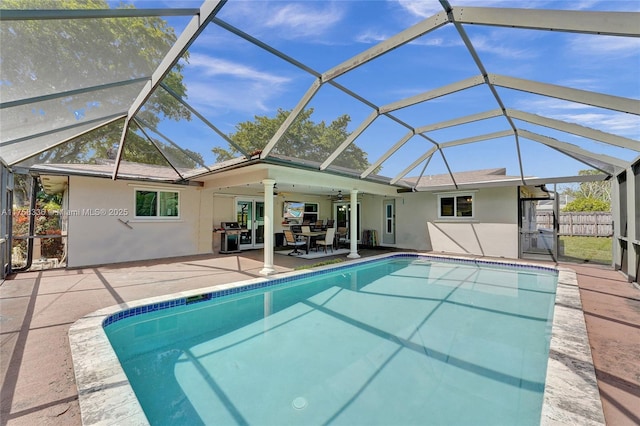 outdoor pool featuring glass enclosure, a patio, fence, and ceiling fan