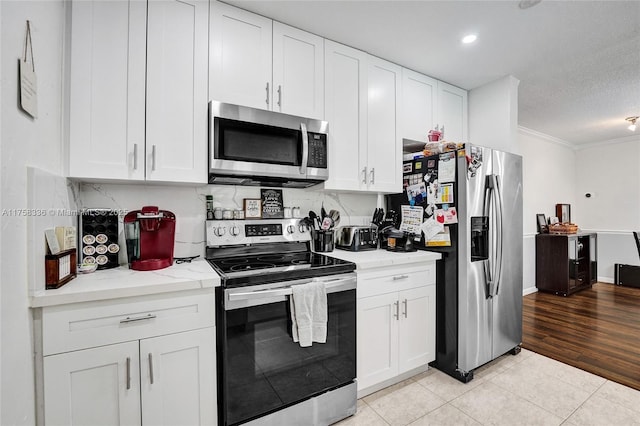 kitchen with white cabinetry, light tile patterned floors, appliances with stainless steel finishes, and ornamental molding