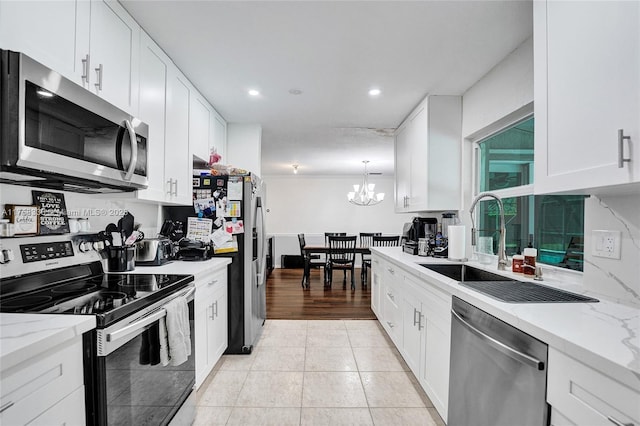 kitchen featuring light tile patterned floors, light stone counters, stainless steel appliances, white cabinetry, and a sink