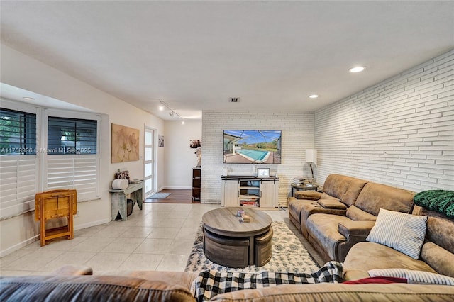 living room featuring visible vents, baseboards, light tile patterned flooring, brick wall, and rail lighting