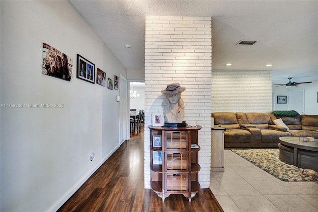 hallway with wood finished floors, baseboards, visible vents, brick wall, and a textured ceiling