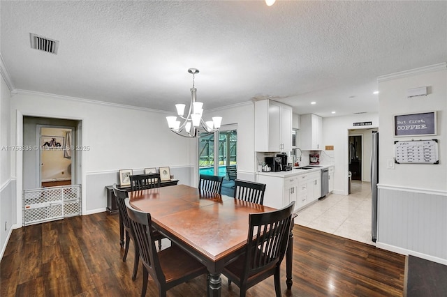 dining area featuring light wood-style floors, ornamental molding, visible vents, a notable chandelier, and a textured ceiling