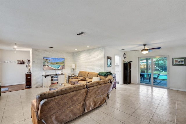 living area with light tile patterned floors, ceiling fan, brick wall, visible vents, and baseboards