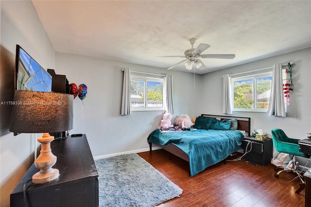 bedroom with wood finished floors, a ceiling fan, baseboards, and multiple windows