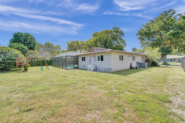 rear view of property featuring a playground, an outdoor pool, stucco siding, glass enclosure, and a lawn