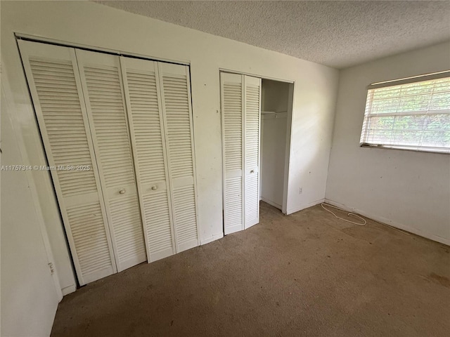 unfurnished bedroom featuring carpet floors, two closets, and a textured ceiling