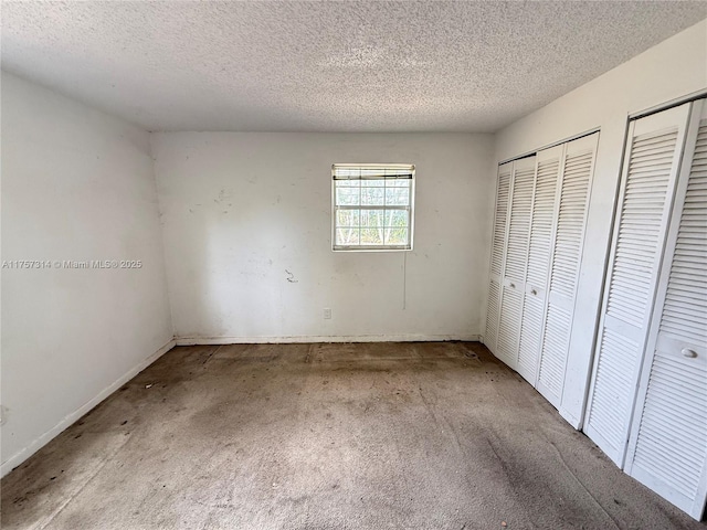 unfurnished bedroom with a textured ceiling, carpet, and multiple closets