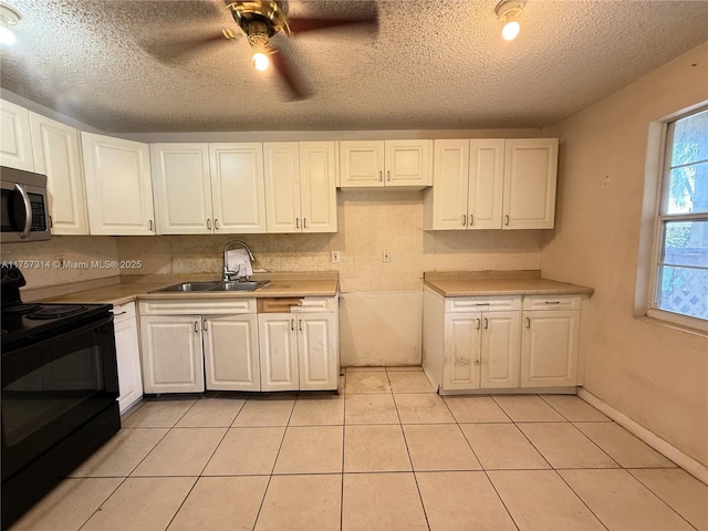 kitchen featuring a sink, white cabinets, light countertops, black electric range oven, and stainless steel microwave