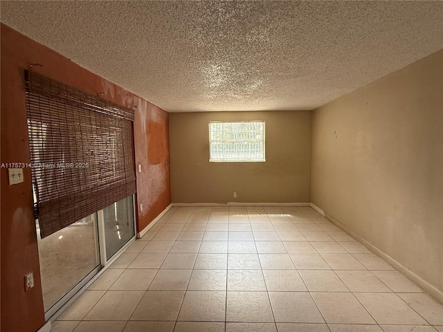 unfurnished room with a textured ceiling, light tile patterned floors, and baseboards