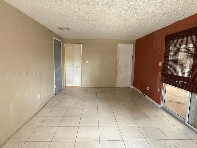 spare room featuring visible vents, a textured ceiling, and light tile patterned floors