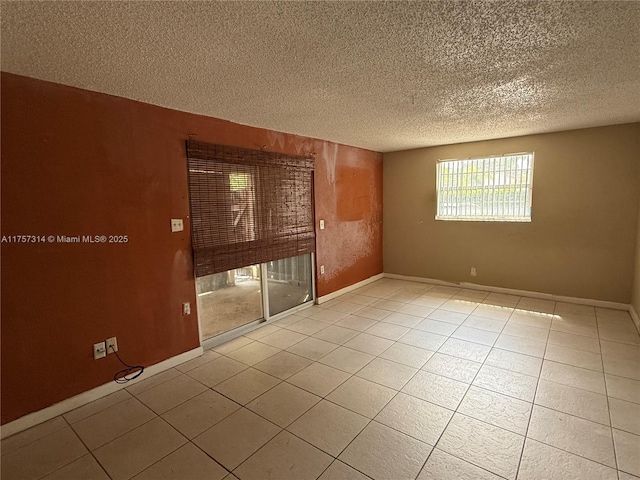 empty room with baseboards, a textured ceiling, and light tile patterned flooring