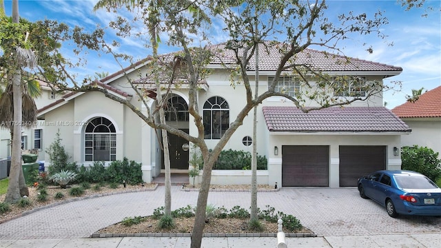 mediterranean / spanish-style home with a garage, decorative driveway, a tile roof, and stucco siding