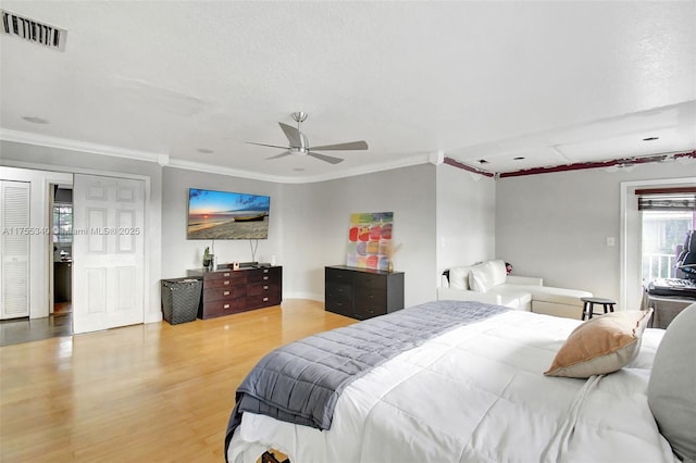 bedroom with ceiling fan, a textured ceiling, wood finished floors, visible vents, and ornamental molding